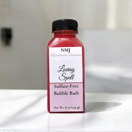 NMJ Handmade Creations sulfate-free bubble bath in 'Loving Spell', presented in a clear bottle with rich red contents and a two-tone pink label, against a serene white bathroom background.