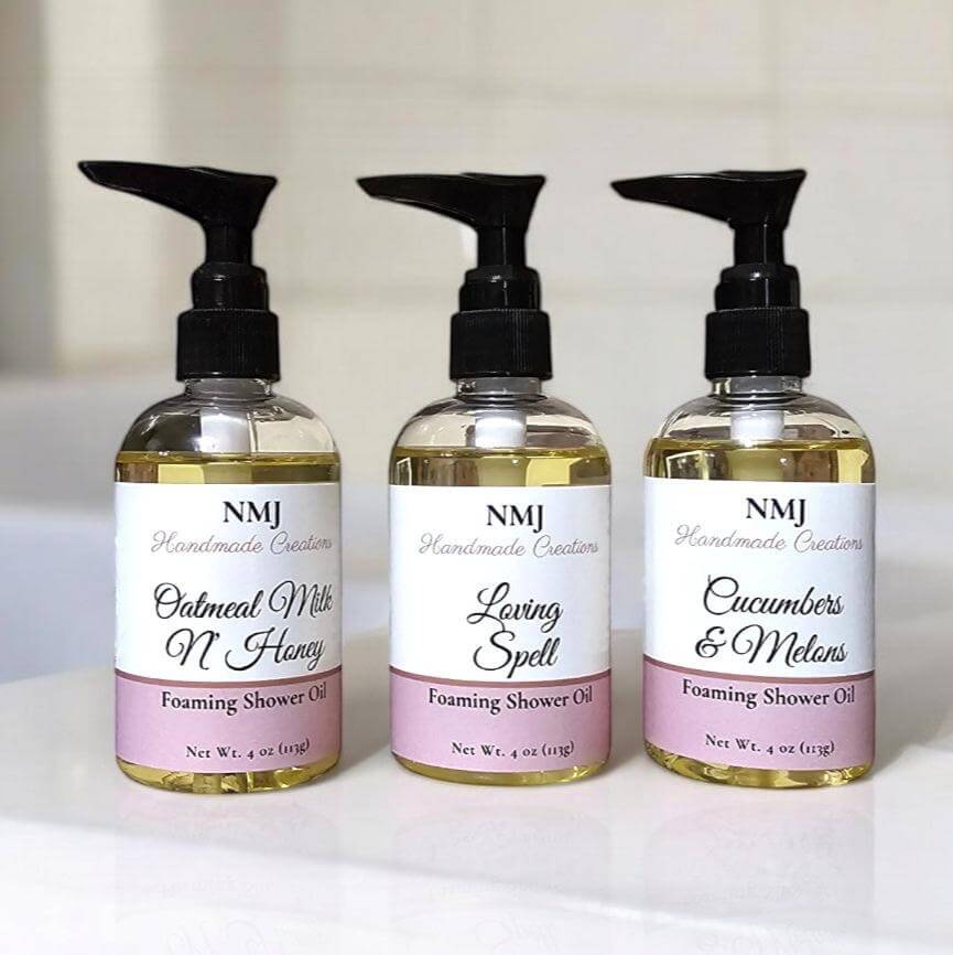 Three bottles of NMJ Handmade Creations Foaming Shower Oil in different scents on a bathroom shelf.