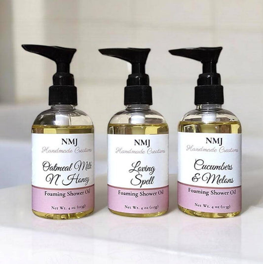 Three bottles of NMJ Handmade Creations Foaming Shower Oil in different scents on a bathroom shelf.