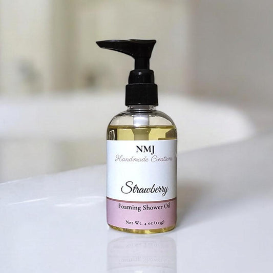 A sleek bottle of NMJ Handmade Creations Strawberry foaming shower oil, featuring a clear bottle with a black pump dispenser, elegantly presented on a bright, reflective white bathroom counter.