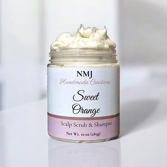 A jar of NMJ Handmade Creations' Sweet Orange Scalp Scrub & Shampoo, featuring a lush white cream, set against a sleek, modern bathroom background.