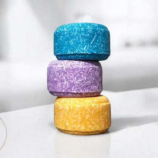 Stack of three jumbo Shampoo bars in vibrant colors of blue, purple, and yellow, displayed against a sleek bathroom backdrop. Each bar features a unique fibrous texture, showcasing an eco-friendly and visually striking alternative for hair care.